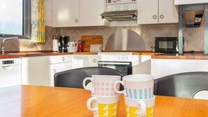 Une cuisine avec des meubles blancs, un four à micro-ondes et une machine à café. Il y a deux tasses sur une table en bois.