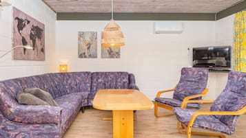A room with a sectional sofa, a round wooden table, two armchairs, a television, and artwork on the walls.