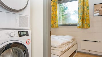 Una habitación funcional con lavadora, cama y ventana con cortinas.