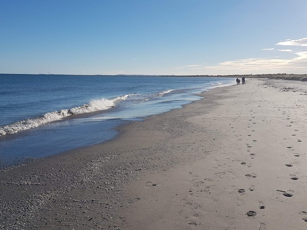A beach with a pebbly shore, a clear sky, and footprints leading to the water.