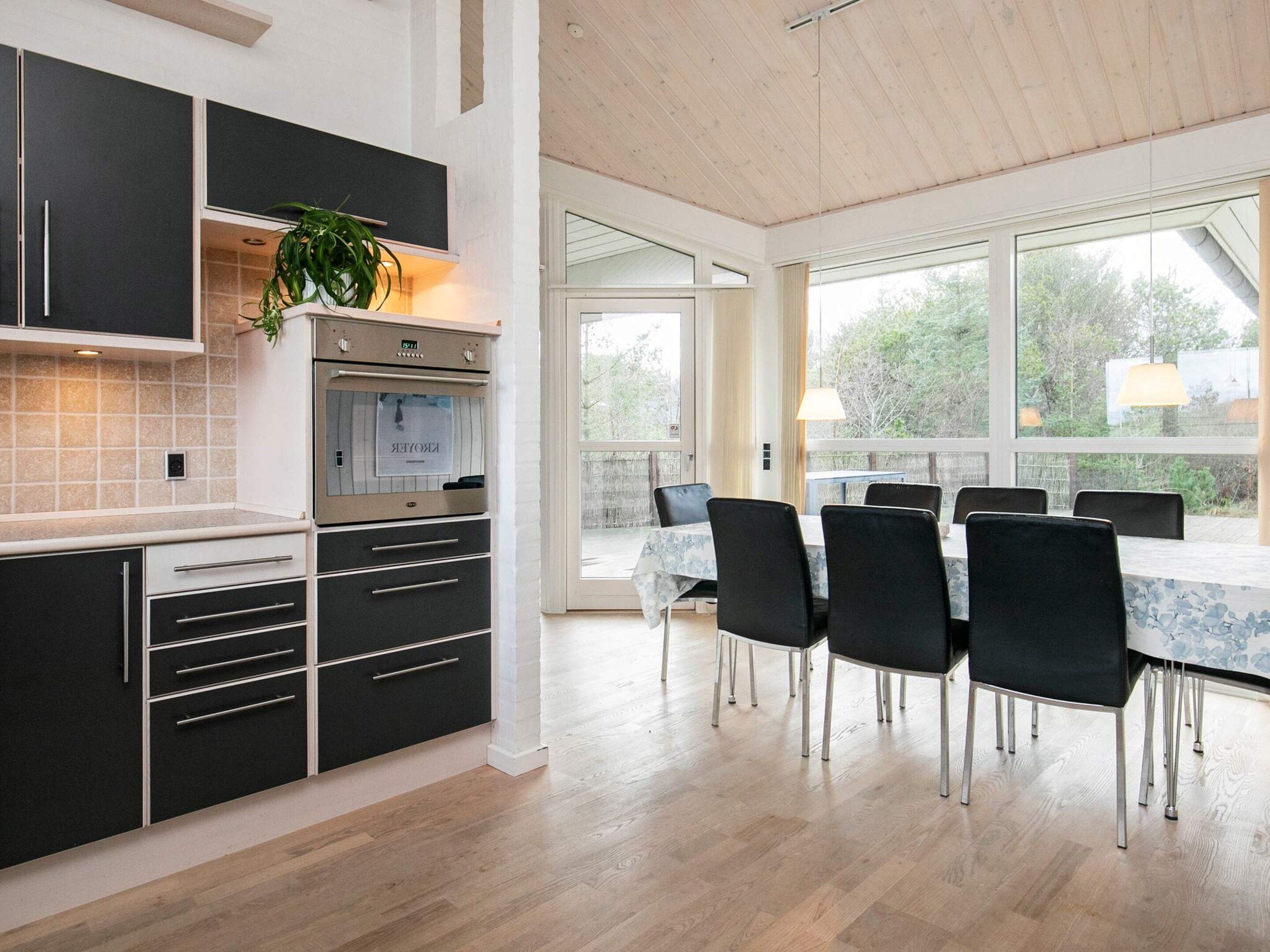 A modern kitchen with black cabinets, a built-in oven, and a dining area with a table and chairs.