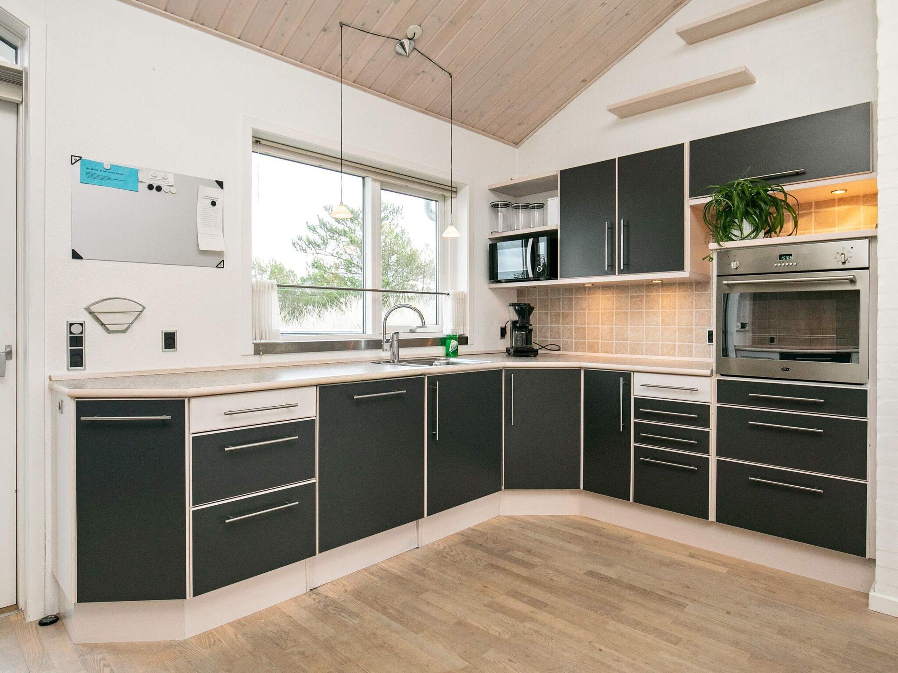 A modern kitchen with black cabinets, a microwave, an oven, and a window providing natural light.