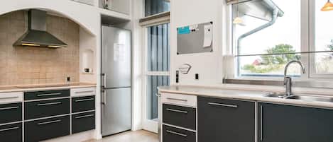 A modern kitchen with a built-in refrigerator, a window with a view, and a wooden ceiling.