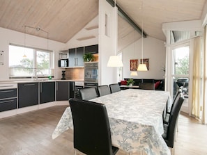 A modern kitchen with a dining area, large windows, and a high ceiling.