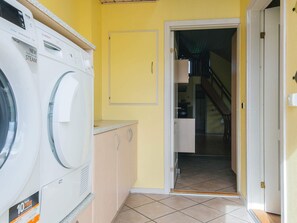 A laundry area with a washing machine and dryer, a door leading to a staircase, and a tiled floor.