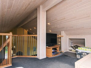 A room with a wooden ceiling, a television, a sofa, and a staircase.