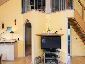 A modern living room with a flat-screen TV, wooden entertainment unit, and a staircase leading to an upper level.