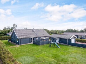 En rad blå stugor med taklagda tak, en gräsyta och en lekplats med en rutschkana.