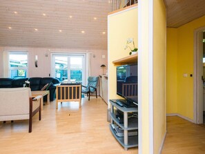 A spacious living room with a wooden ceiling, a black leather sofa, a light blue armchair, and a wooden coffee table.