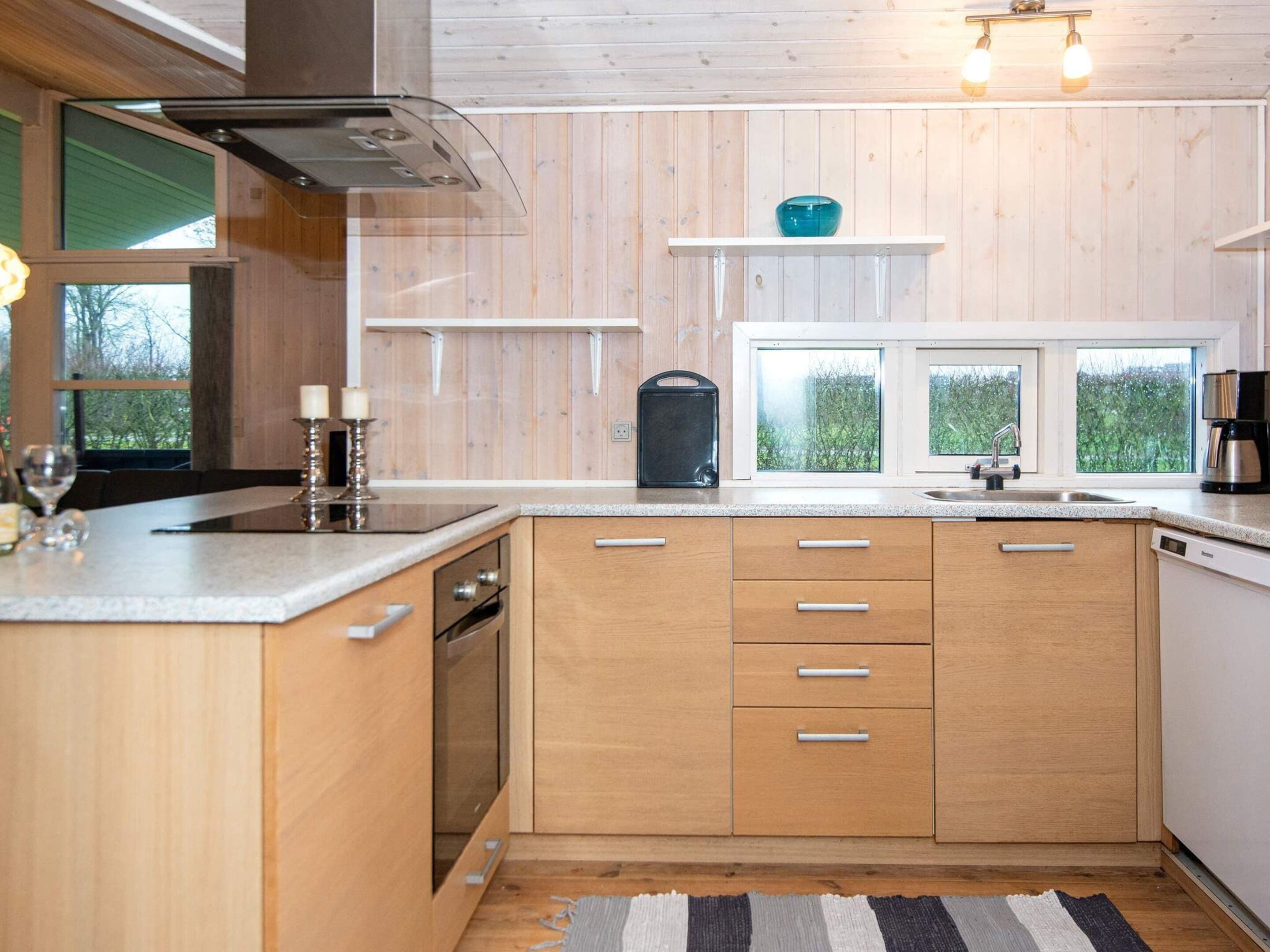 Une cuisine moderne avec des meubles en bois, un four encastré, un lave-vaisselle et une fenêtre donnant sur un paysage verdoyant.