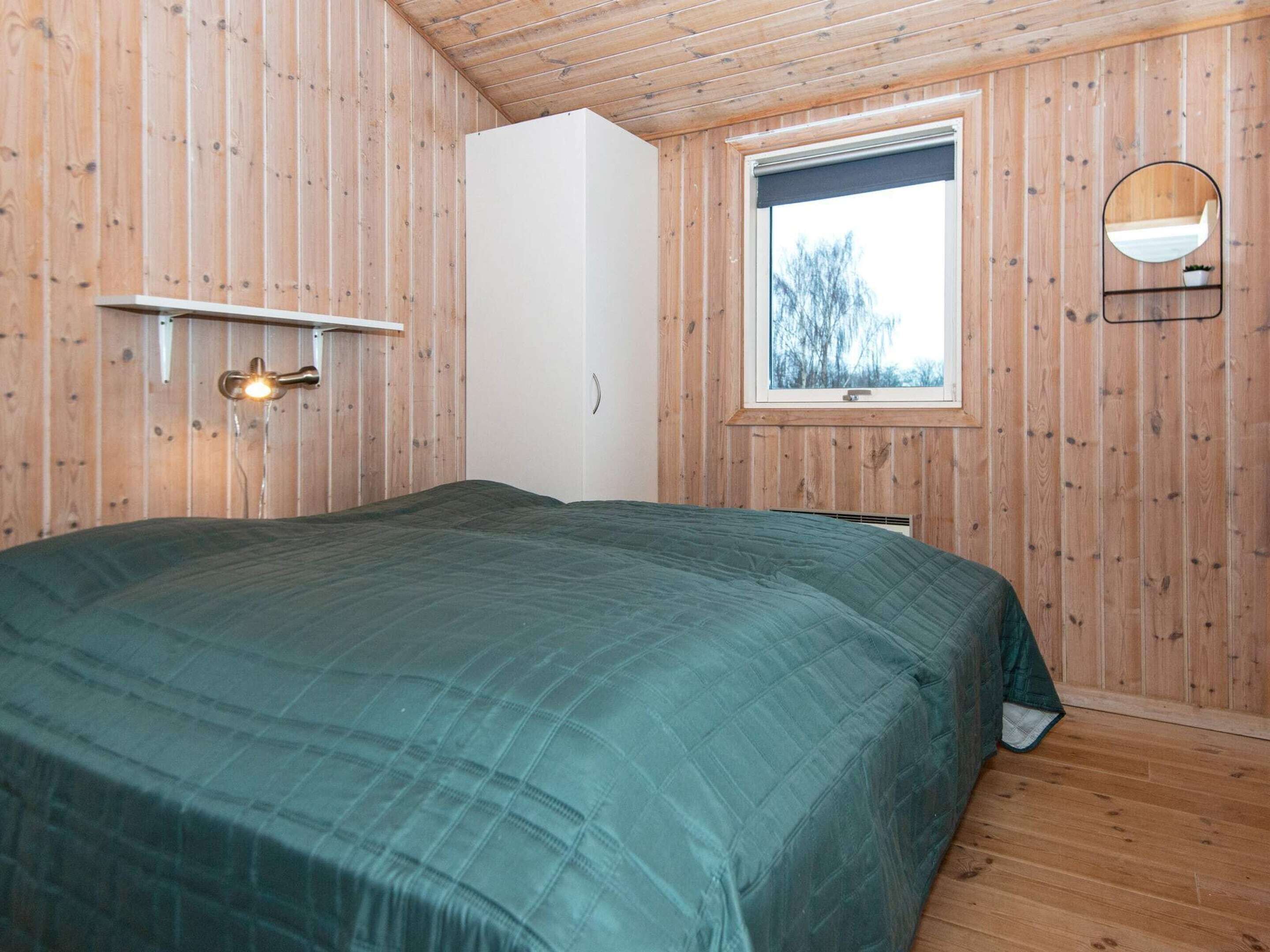 A bedroom with a bed, a window, a mirror, and wooden walls.