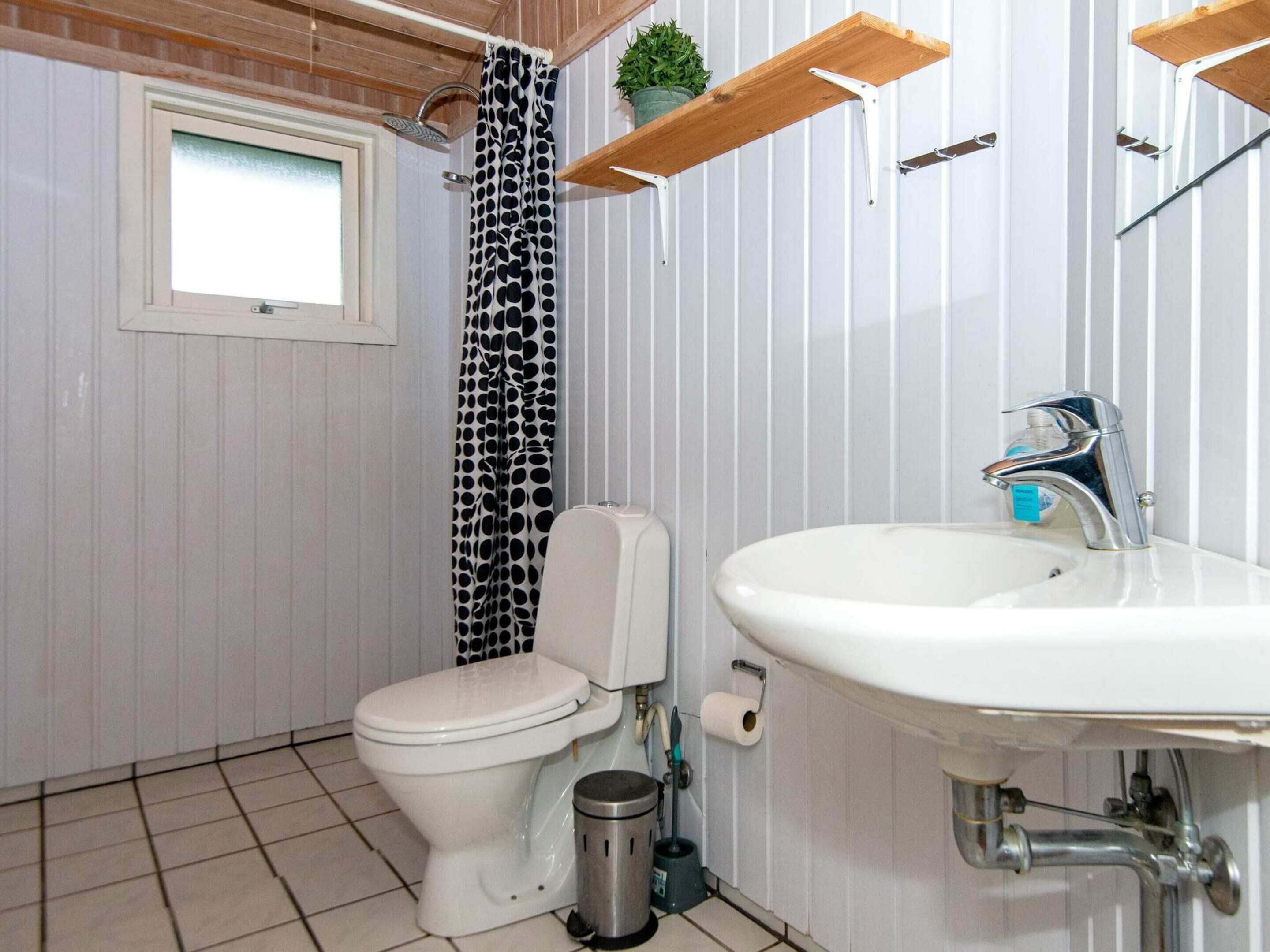 A bathroom with a toilet, sink, shower, and a window.