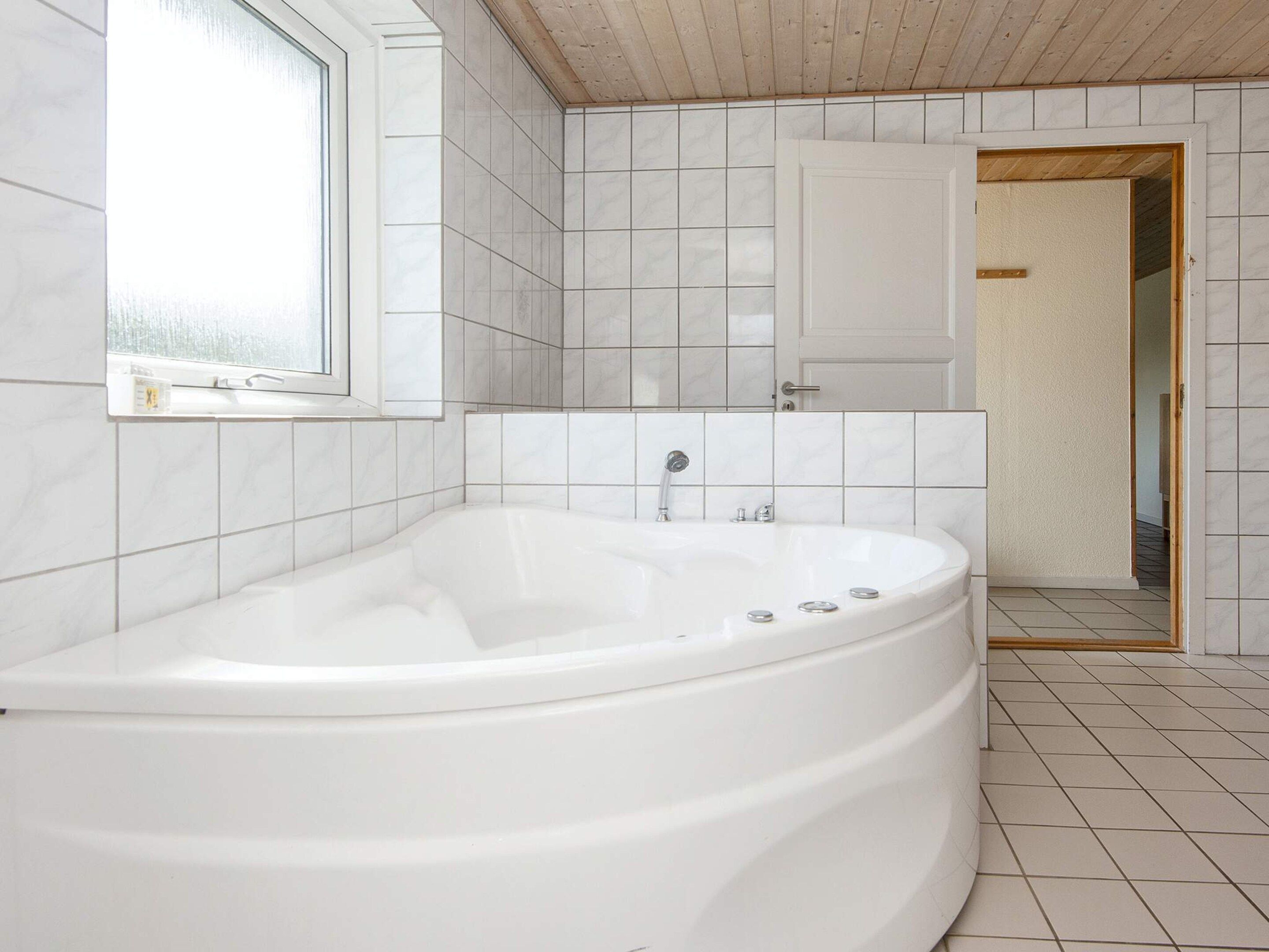 A modern bathroom with a freestanding bathtub, white tiled walls, and a wooden ceiling.