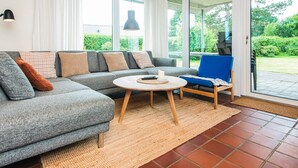 A modern living room with a grey sectional sofa, a round coffee table, and a blue armchair. - Holiday Home in Odder (Odder)