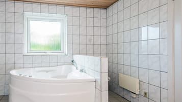 A bathroom with a freestanding bathtub, a window, and tiled walls.