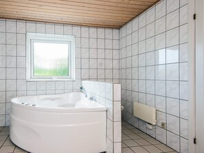 Een badkamer met een vrijstaand bad, een raam en betegelde muren.
