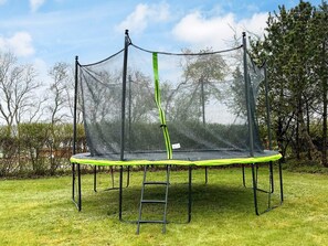 A trampoline with a safety net, surrounded by grass and trees. - Holiday Home in Odder (Odder)