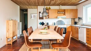 A modern kitchen with wooden cabinets, a central island, and a dining area with chairs. - Holiday Home in Odder (Odder)