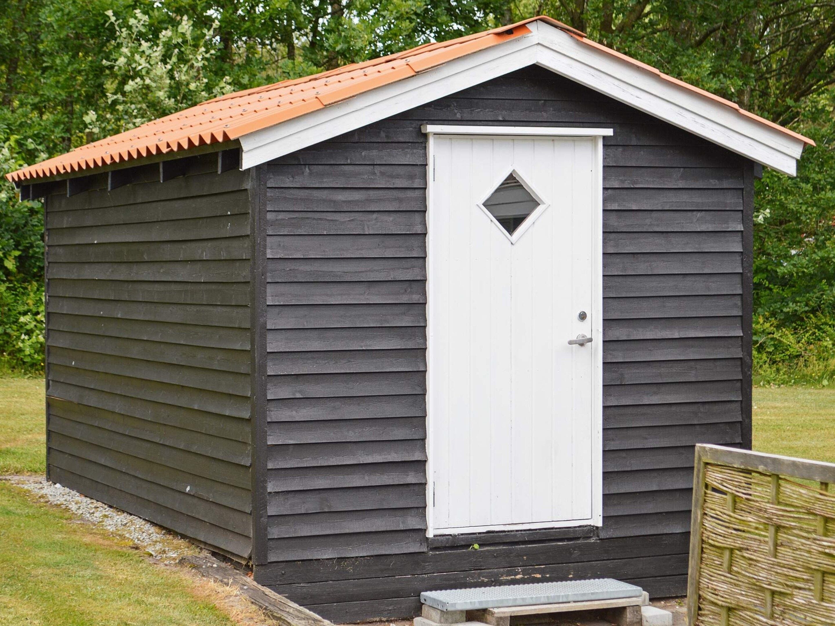 A small, dark wooden shed with a white door and a red roof.