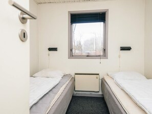 Una camera d'albergo piccola e singola, con due letti, una finestra con persiane, un termosifone e una porta con maniglia.