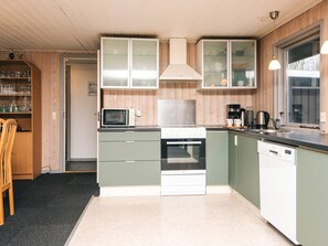 A compact kitchen with a microwave, stove, oven, and dishwasher. There is a wooden chair and a cabinet with glass doors. - 6 Person Holiday Home in Toftlund (Toftlund)