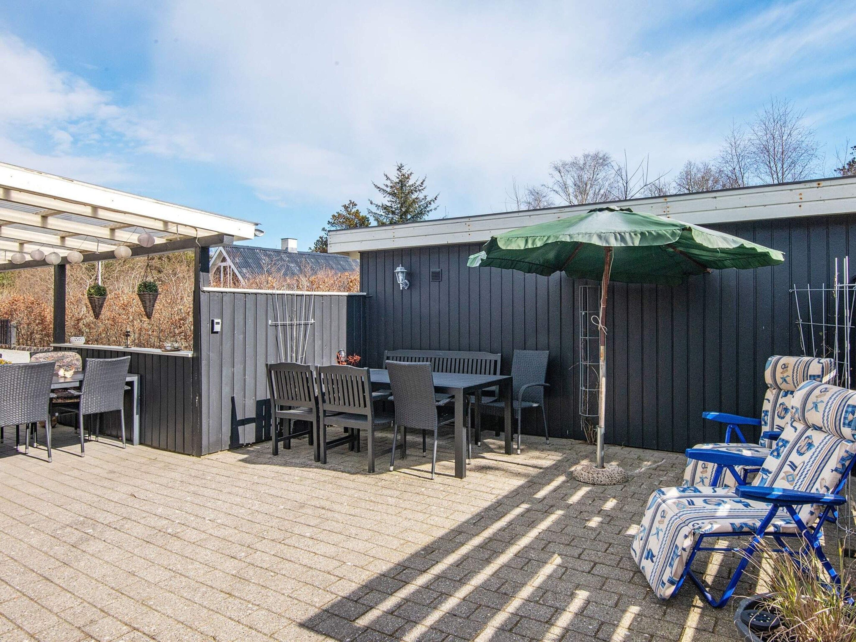 Eine Terrasse mit Tisch und Stühlen, einem Hängesessel und einem grünen Sonnenschirm.