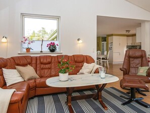 A living room with a brown leather sofa, a round coffee table, and a dining area in the background. - 8 Person Holiday Home in Logstor (Logstor)