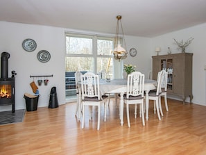 A dining room with a white table, chairs, a chandelier, a fireplace, and a view through a large window. - 8 Person Holiday Home in Logstor (Logstor)
