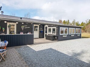 A building with a covered patio area, a seating arrangement, and a grill outside.