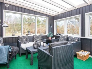 A sunroom with wicker furniture, large windows, and a view of trees.