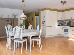 A dining area with a round table and chairs, a hanging light fixture, and a kitchen with cabinets and appliances. - 8 Person Holiday Home in Logstor (Logstor)