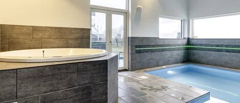 A modern bathroom with a freestanding bathtub, a glass-enclosed pool, and a large window providing natural light.