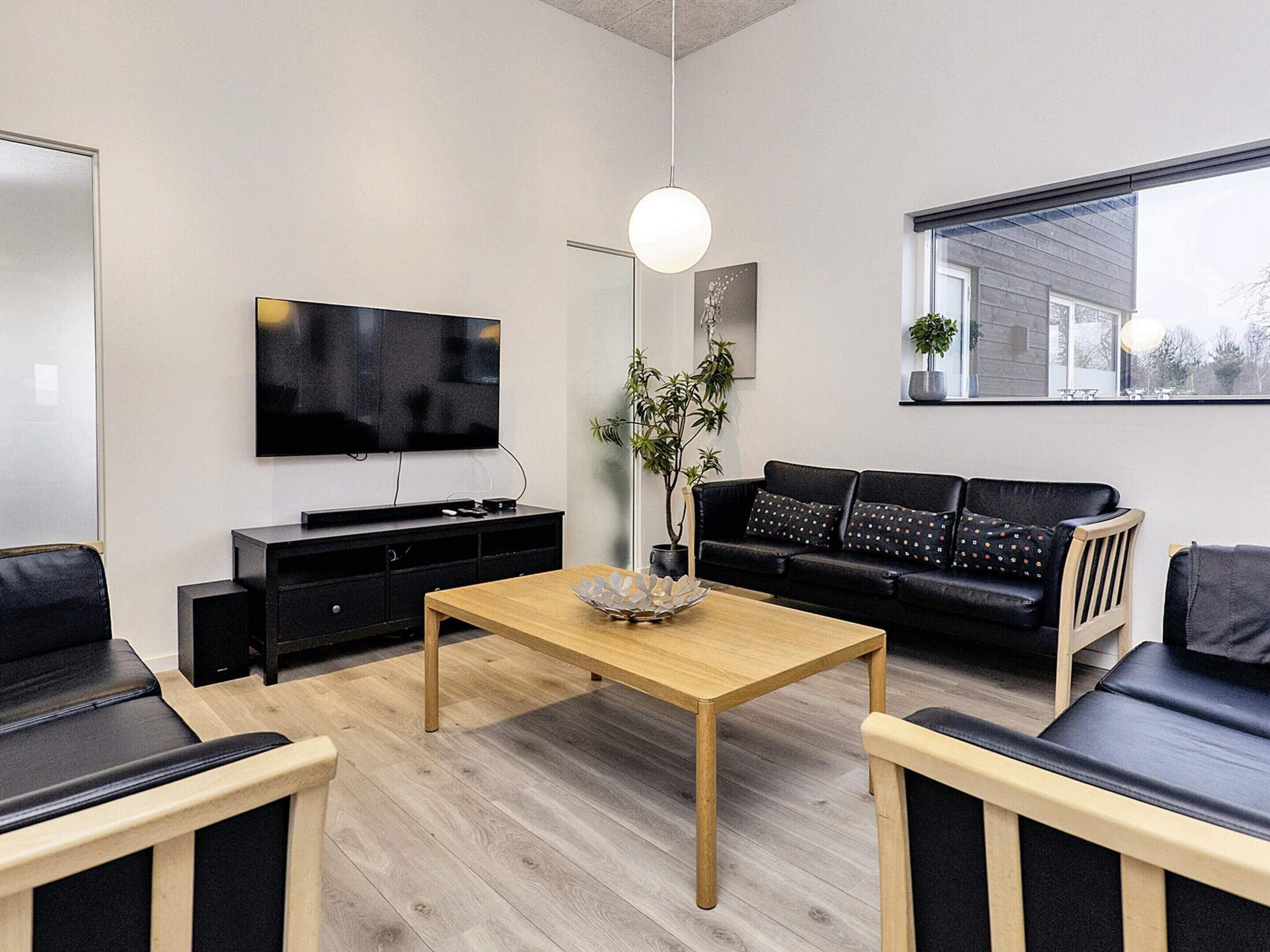 Ett modernt vardagsrum med en platt-TV, ett soffbord i trä, en svart soffa och en svart fåtölj.
