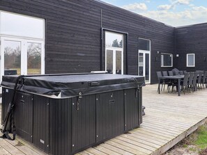 Un hidromasaje exterior negro en una terraza de madera, con una mesa y sillas cerca.
