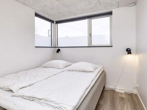 A bedroom with a bed, a window, and a wall-mounted lamp. - Holiday Home in Væggerløse (Vaeggerlose)