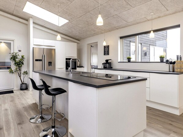 A modern kitchen with a central island, bar stools, stainless steel appliances, and pendant lighting.