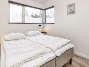 A bedroom with a bed, a nightstand, a wall-mounted lamp, and a window.