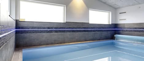 En moderne indendørs swimmingpool med blå bund, to vinduer og en væg med et blå- og sort flisemønster.