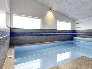 A modern indoor swimming pool with a blue floor, two windows, and a wall with a blue and black tile pattern.