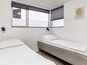 Un dormitorio con dos camas individuales, una ventana con persianas, una lámpara de pared y una obra de arte enmarcada.