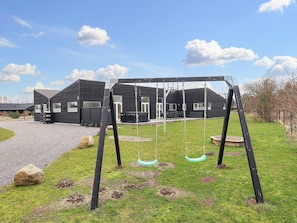 A playground with swings and a building in the background. - Holiday Home in Væggerløse (Vaeggerlose)