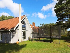 A house with a red-tiled roof, a chimney, and a trampoline in the yard.