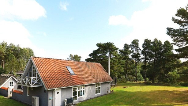 Une maison à deux étages, avec un toit recouvert de tuiles rouges, un balcon et une cour gazonnée.