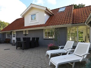A house with a tiled roof, a patio with a table and chairs, and two lounge chairs. - 8 Person Holiday Home in Hals (Hals)