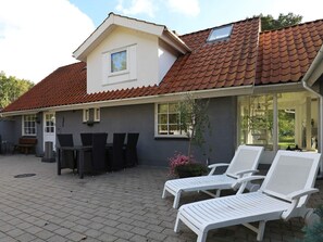 Ett hus med ett tak täckt av takpannor, en uteplats med ett bord och stolar samt två solstolar.