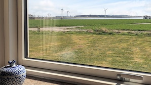A window view of a green field with wind turbines in the distance. - 8 Person Holiday Home in Harpelunde (Harpelunde)