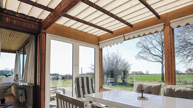 A covered patio with a table and chairs, large windows offering a view of the countryside. - 8 Person Holiday Home in Harpelunde (Harpelunde)
