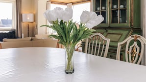 A dining table with a clear glass vase containing white flowers, a green cabinet with glass doors, and a window with curtains. - 8 Person Holiday Home in Harpelunde (Harpelunde)