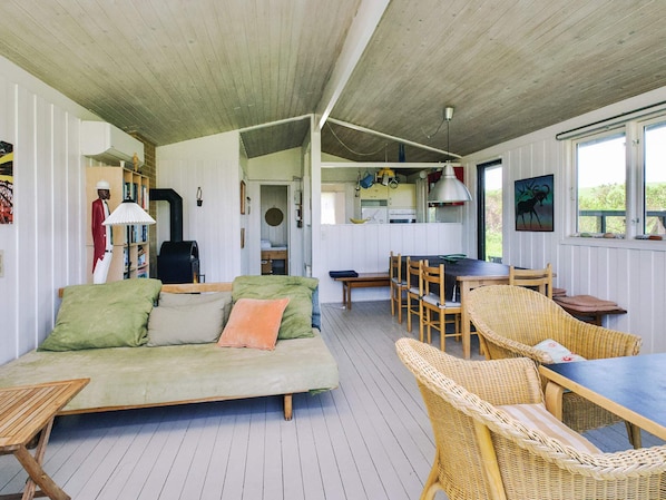 Un espacio acogedor con sofá, mesa de comedor, sillas de mimbre, zona de cocina y un ventanal grande.