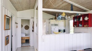 A compact, well-organized room with a kitchenette, a bed with storage, and a seating area with cushions.